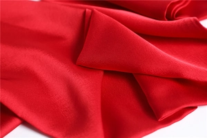 Detailed close-up of smooth red satin scarf fabric with elegant folds and glossy texture