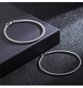 Detail of silver wheat chains with lobster clasps on high-contrast black textured background