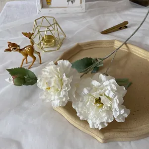Detail of three-headed white artificial peonies on a beige octagonal tray with green leaves