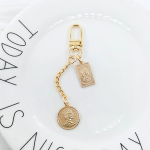 Golden pearl chain keychain with vintage coin and portrait pendant on ceramic tray