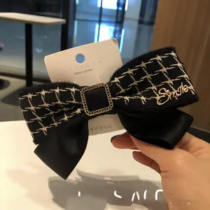 Détail d'une barrette nœud en tweed noir vintage avec lettrage Smile doré et chaîne