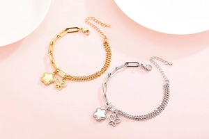 Dettaglio di bracciali in acciaio al titanio oro e argento con ciondoli a fiore e farfalla
