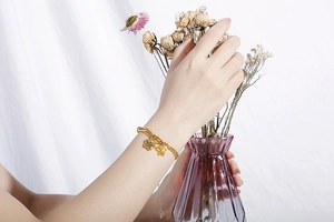Dettaglio del bracciale placcato oro con ciondoli a fiore e farfalla sul polso della modella