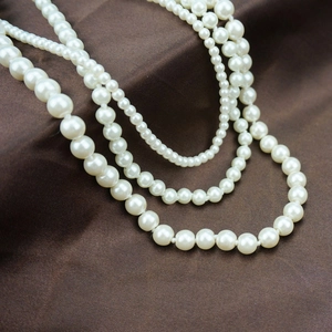 Detailed view of layered cream white faux pearl necklace on elegant brown silk fabric