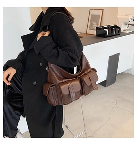 Detail of a dark brown multi-pocket leather tote bag worn by a model in a cafe setting