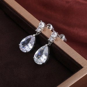 Macro shot of silver-colored pear-cut zircon teardrop earrings on dark velvet