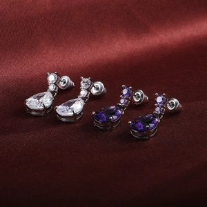 Macro detail of teardrop cubic zirconia earrings in clear and purple on red silk