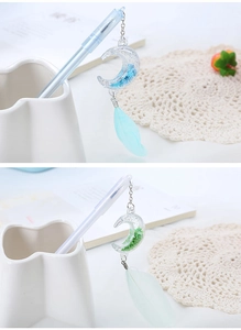 Close-up of creative gel pen with blue and green moon-shaped liquid sand charm and feather
