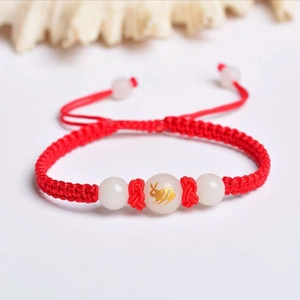 Close-up of handmade red braided bracelet with luminous white beads and golden rabbit charm
