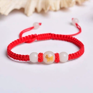 Macro view of handmade red braided bracelet with a glowing goat zodiac bead and white stones