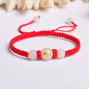 Macro shot of red braided bracelet featuring a luminous white jade bead with a gold rat motif