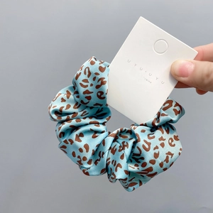 Close-up of light blue leopard print scrunchie with satin texture on display card
