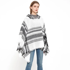 Dettaglio del poncho con cappuccio, motivi a scacchi neri e bianchi e finiture con frange