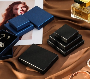 Various sizes of black and navy blue jewelry gift boxes on elegant brown silk background