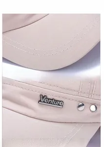 Close-up of beige flat top cap featuring metal Venture logo and precise stitching details