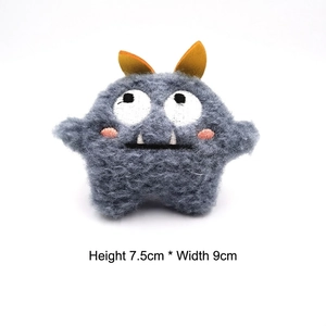 Detail showing grey plush monster brooch dimensions of 7.5cm height and 9cm width