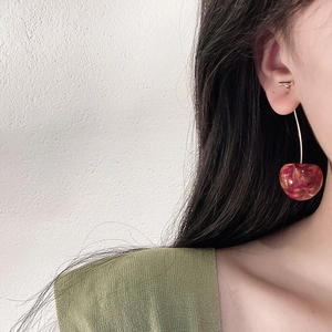 Close-up of model wearing vibrant red cherry earrings with elegant gold hooks