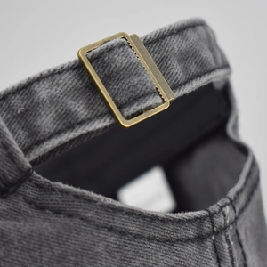 Detail view of washed gray denim baseball cap with vintage bronze metal buckle closure
