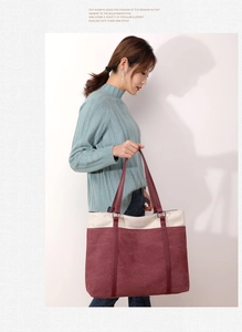 Detail view of a large burgundy and cream canvas tote bag held by a model for daily use