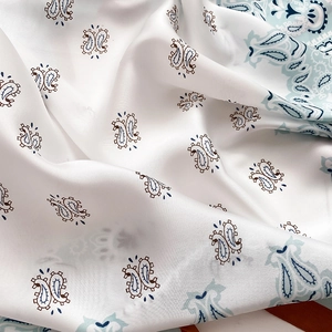 Close-up of paisley pattern on smooth white satin fabric with soft silk texture