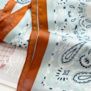 Detailed macro view of light blue paisley silk scarf with satin texture and caramel border