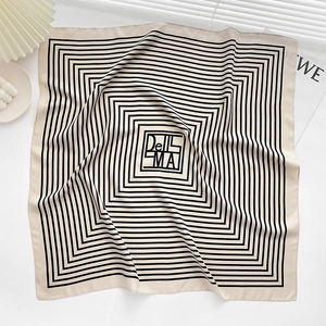 Macro detail of a beige silk scarf featuring black square patterns and logo lettering