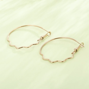 Elegant gold wavy hoop earrings with minimalist metal finish on pale green background