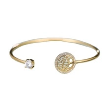 Detail of gold open bracelet featuring Tree of Life charm and clear round gemstone