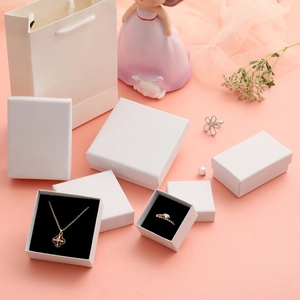 White textured paper jewelry boxes with handles and black foam inserts on pink background
