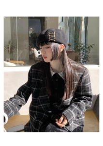 Detail of a black wool beret with golden metal buckles on a model in a plaid blazer