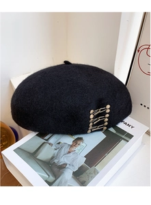 Detail view of black wool beret with three gold metal buckles on a book background