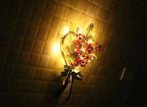 Illuminated heart-shaped rattan wreath with red berries, pine needles and warm LED lights