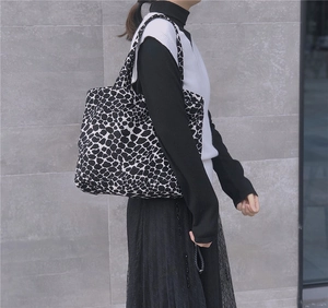Detail of a cow print canvas tote bag with long handles styled on a casual model