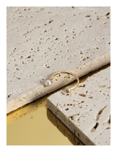 Macro shot of minimalist gold pearl and zircon ring on textured stone with mirror reflection