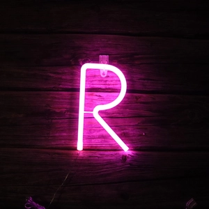 Close-up of pink neon letter R light sign mounted on a dark vintage wooden wall texture