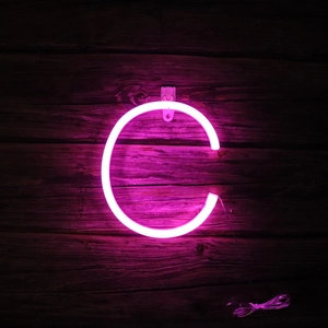 Close-up of pink LED neon letter C light hanging on dark wood wall for room decoration