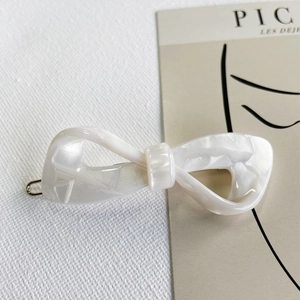 Close-up of a white pearlescent acetate bow hair clip with a metallic base on a card