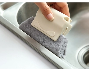 Detail of beige handheld groove cleaning brush scrubbing a stainless steel sink edge