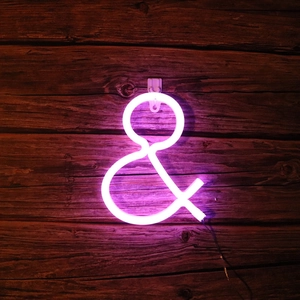 Close-up of pink-purple LED neon ampersand symbol glowing on a rustic dark wood wall