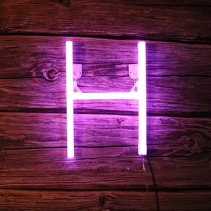 Close-up of pink purple LED neon letter H on rustic dark wood background for party decor