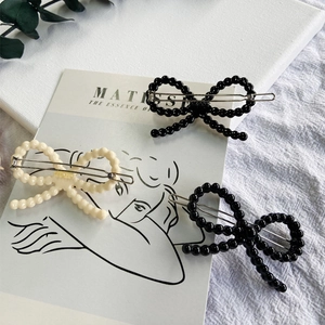 Close-up of elegant beaded bow hair clips in cream and black on an artistic background