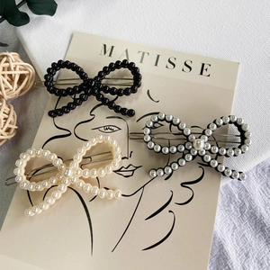 Detailed view of three handcrafted pearl bow hair clips in black and cream finishes