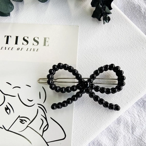 Detail of black beaded bow hair clip on a minimalist card with artistic dry leaves