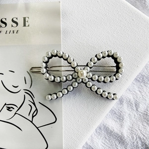 Detailed view of an elegant pearl bow hair clip with silver metal frog clip base