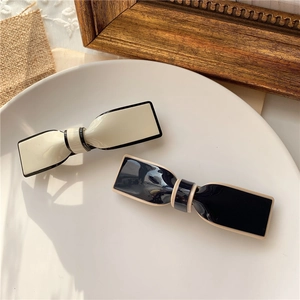 Elegant bow hair clips in black and cream finish displayed on a white ceramic plate