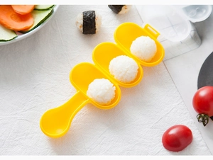 Three-slot yellow plastic rice ball mold with long handle on a styled kitchen table
