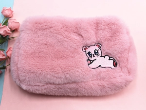 Gros plan d'une trousse à maquillage rose en peluche avec ours brodé sur fausse fourrure