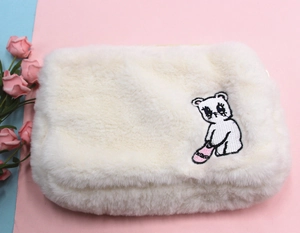 Détail de la trousse de maquillage blanche en peluche avec broderie d'ours et texture douce