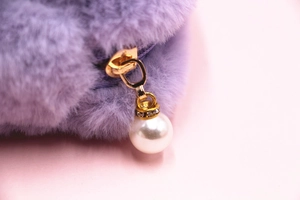 Détail de la trousse de maquillage en peluche violette avec fermeture dorée et perle