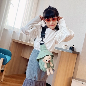 Green canvas kids crossbody bag with plush bear pendant worn by a young girl